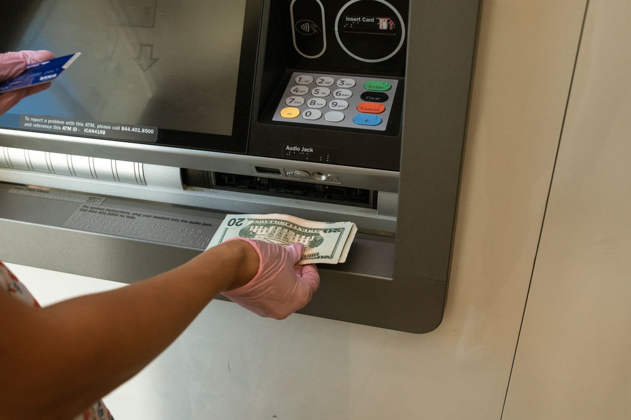 services-04 A person wearing gloves withdrawing cash from an ATM machine showcasing money handling and hygiene.