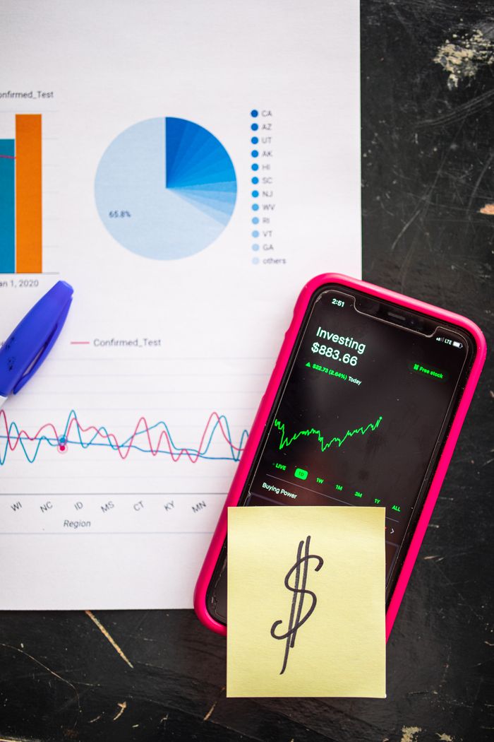 services-02 Smartphone displaying stock market data alongside financial charts and a dollar sign note.
